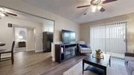 This single-story, 2-bedroom, 1-bathroom unit offers a well-organized floor plan that efficiently utilizes its compact footprint. The living room serves as the central gathering space, featuring wood-style plank flooring, a textured ceiling, and a ceiling fan with light fixture. A sliding glass door fitted with vertical blinds allows natural light into the room and provides outdoor access. The living area flows visibly into the dedicated dining nook, which is defined by a recessed ceiling detail and includes its own ceiling fan. Adjacent to the dining area, the galley-style kitchen is outfitted with white cabinetry, gray laminate countertops, and black appliances, including a refrigerator, range, microwave, and dishwasher. A window at the end of the kitchen draws in additional natural light. A hallway with an arched architectural detail connects the main living areas to the two bedrooms and shared bathroom. The bedrooms feature carpet flooring and sliding closets. The full bathroom includes a single-sink vanity with white cabinetry, gray countertop, and a tub-shower combination. Wood-style flooring continues throughout the bathroom and common areas, providing a cohesive aesthetic across the unit.