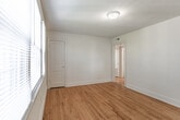 Located at 312 73rd St in Newport News, Virginia, this single-floor residence offers a straightforward and functional layout with consistent design details throughout. Warm-toned hardwood floors run through the living areas and bedrooms, lending a classic character to the interior. The living space provides a clean, open feel with neutral white walls and ceiling-mounted lighting. Multiple rooms benefit from natural light streaming through windows fitted with blinds, offering views of the surrounding neighborhood. The bedrooms are well-proportioned, with one featuring a closet and a wide multi-pane window that brightens the space considerably. The kitchen is equipped with oak cabinetry, dark laminate countertops, a stainless steel sink, and white appliances including an electric range and an over-the-range microwave, all set atop tile flooring. The bathroom is neatly appointed with tile flooring, a white vanity with medicine cabinet, a tub-shower combination, and classic black tile accent trim. White walls and bright vanity lighting keep the space feeling clean and functional. The overall ambiance of the home is practical and inviting, with a cohesive neutral palette and durable finishes throughout.
