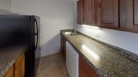 This two-floor residence offers a well-organized layout with distinct living areas across both levels. The kitchen is equipped with dark granite countertops, rich wood cabinetry, a stainless steel sink, a dishwasher, and a refrigerator, all set atop tile flooring that adds a clean, practical finish to the space. A white-painted staircase with classic baluster railings connects the two floors, serving as both a functional and architectural element of the home. The upper level features an open loft area distinguished by angled, vaulted ceilings that lend a sense of height and character to the space. Warm, neutral carpeting runs throughout the upper floor, creating a comfortable and cohesive atmosphere. A separate carpeted room on the upper level showcases white board-and-batten wall paneling and a window overlooking greenery outside, bringing in natural light and a touch of charm. The bathroom is straightforward and functional, finished in neutral gray tones with a full tub and shower combination, a toilet, and clean white fixtures. Throughout the space, a neutral color palette of whites and grays provides a calm, versatile backdrop suited to a variety of interior styles.