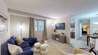 Located at 7779 New York Ln in Glen Burnie, MD, this one-bedroom, one-bathroom residence offers a thoughtfully designed single-floor layout with a cohesive, modern aesthetic throughout. The welcoming entrance opens into a combined living and dining area, where soft carpet flooring, neutral walls, and natural light from large windows create a bright and comfortable atmosphere. The living room features a classic blue sofa, vibrant accent rug in gold and grey tones, and a wall-mounted television, while the adjacent dining space is anchored by a bold blue accent wall with an ornate mirror and a rich wood sideboard, adding a distinct design flair. The kitchen is equipped with dark wood cabinetry, a gas range, refrigerator, and under-mount sink, complemented by light hardwood-style flooring and a window that brings in natural light. The generously sized primary bedroom offers plush carpeting, warm neutral tones, a standout accent wall, and dual reach-in closets providing ample storage, along with windows dressed in teal curtains that add a serene touch. The full bathroom includes a combination tub and shower with a window for natural ventilation. Every room reflects a consistent, tasteful design with carefully chosen furnishings and artwork throughout.