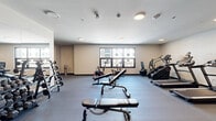 Located at 900 3rd St SE in Cedar Rapids, Iowa, this fitness center spans a generous single floor divided into two dedicated exercise rooms, offering a well-rounded environment for a variety of workout routines. The space features a clean, modern design with neutral-toned walls, durable rubberized flooring, and recessed lighting throughout, creating a bright and functional atmosphere.

The primary exercise room is the larger of the two and is outfitted with an impressive selection of strength training equipment, including a full rack of dumbbells, adjustable weight benches, and a multi-functional cable machine. Large mirrors line one wall, enhancing the sense of space and allowing users to monitor their form. A water fountain is conveniently accessible within this area. Cardio equipment — including treadmills, an elliptical, and a stationary spin bike — is positioned near windows that overlook the surrounding Cedar Rapids streetscape, allowing natural light to fill the room.

The second exercise room offers a more flexible, open layout suited for functional fitness and group-style training. It includes a wall-mounted mirror, yoga mats, resistance equipment, a stability ball, and a step platform. A window provides natural light and views of the neighboring cityscape. Together, the two rooms create a comprehensive fitness facility designed to accommodate a wide range of exercise disciplines.
