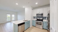 Located at 1502 Benton Blvd in Savannah, GA, this single-floor, 2-bedroom, 1-bathroom home offers a thoughtfully designed layout that maximizes functionality and style. The kitchen serves as the heart of the home, showcasing a two-tone design with soft blue-gray lower cabinets and crisp white upper cabinets, complemented by a blue subway tile backsplash. A peninsula with a white quartz countertop and double sink provides additional prep space, while stainless steel appliances — including a refrigerator, range, microwave, and dishwasher — complete the modern setup. Light hardwood-style flooring runs throughout the kitchen and living areas, enhancing the bright, airy feel. Both bedrooms are carpeted and feature ceiling fans and large windows with blinds that invite natural light and offer views of the surrounding greenery. The primary bedroom includes a spacious walk-in closet with wire shelving for generous storage. The bathroom is clean and contemporary, featuring a tub-shower combination, a light blue vanity with quartz countertop, a large framed mirror, and light wood-tone flooring. The overall palette of whites, soft blues, and warm neutrals gives the home a cohesive, welcoming ambiance throughout.