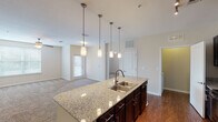 This thoughtfully designed 2-bedroom, 2-bathroom residence in Spring, Texas offers a comfortable and functional single-floor layout. The kitchen serves as the heart of the home, featuring a large granite-topped center island with a double stainless steel sink, dark espresso cabinetry, black appliances including a refrigerator, electric range, and built-in microwave, and rich hardwood-style flooring. Pendant lighting and a track light fixture illuminate the space with a warm, inviting glow that flows seamlessly into the open living area, which is finished with plush carpeting. Both bedrooms are generously proportioned, each appointed with ceiling fans, plush carpet, and ample natural light from multiple windows. The bathrooms feature dark vanity cabinetry with white countertops, and one bathroom includes convenient closet access with built-in wire shelving. A dedicated in-unit laundry room accommodates a full-size washer and dryer side by side. Throughout the residence, neutral warm tones on the walls complement the contrasting dark cabinetry and hardwood-style flooring, creating a cohesive and modern aesthetic. The layout also includes accessible hallways and interior storage, offering both style and practicality.