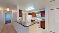This single-floor residence offers a thoughtfully designed layout that balances functionality with comfort. The open-concept living and dining area is finished with large neutral-toned floor tiles, a ceiling fan, and a sliding glass door that allows natural light to pour in and provides access to the outdoors. The kitchen is positioned adjacent to the living area and features rich medium-toned wood cabinetry, granite-style laminate countertops, and a suite of white appliances including a refrigerator, electric range, and over-the-range microwave. A wraparound breakfast bar with a built-in sink connects the kitchen to the living space, making it ideal for casual dining and entertaining. A dedicated pantry closet offers generous storage. The bedrooms are carpeted for comfort and each includes a ceiling fan and windows with blinds that bring in natural greenery views. The bathrooms are finished with light tiles, wood vanities topped with granite-style counters, and chrome fixtures. The full bathroom includes a tub-shower combination with tiled surround and a large vanity mirror. Throughout, the space maintains a clean, neutral palette that provides a versatile and inviting living environment.