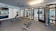Located at 10165 Park Meadows Dr in Lone Tree, Colorado, this well-appointed fitness center is designed to support a comprehensive range of workout disciplines across a single, thoughtfully organized floor. The space is divided into several distinct training zones, each tailored to specific fitness activities.

The spin and cardio studio features eye-catching geometric-patterned flooring in varying shades of gray, complemented by a large wall-to-wall mirror framed in bold black. Blue wall padding and modern ceiling fans round out this focused training environment. Adjacent to this area is a functional training zone with matching geometric flooring, equipped with stability balls, kettlebells, and balance tools, offering direct views to an outdoor courtyard through large black-framed glass doors and windows.

A dedicated free weight and strength training room provides a rubber-floored space housing a power rack and bench press station, with glass doors opening directly to the outdoor patio area, flooding the space with natural light and outdoor views. Another section features a notable "Freedom Climber" rock climbing wall as a standout architectural and fitness element, set against clean white walls with open floor space ideal for functional movement.

Connecting these zones are sleek black-framed glass partition walls that maintain visual openness throughout. Exposed ductwork and linear LED lighting contribute to a modern industrial aesthetic throughout the facility.