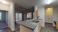 This single-story residence is designed with an open and functional layout that connects the main living areas seamlessly. The kitchen features light wood cabinetry, grey laminate countertops, a double-basin sink, a white appliance suite including a range and refrigerator, and dark wood-look flooring. A peninsula counter separates the kitchen from the spacious living room, which is distinguished by a tray ceiling accented with crown molding and a ceiling fan. The living room opens toward a dining area finished with an elegant pendant light, crown molding, and direct access to a private balcony through a glass-paneled door.

The bedrooms are carpeted and generously sized, each benefiting from multiple windows that invite natural light. One bedroom features dual corner windows and a ceiling fan, while another includes access to a walk-in closet. The primary bathroom offers a dual-sink vanity with an extended countertop, a large mirror, and a bathtub with tiled surround, all set on dark wood-look flooring. A secondary bathroom provides similar finishes with a single-sink vanity and a tub-shower combination. Additional storage is available throughout, including a pantry-style closet off the kitchen corridor.