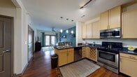 This single-floor residence is designed with an open-concept layout that seamlessly connects the kitchen and living areas. The kitchen is well-equipped with light maple cabinetry, dark granite countertops, stainless steel appliances including a range, built-in microwave, dishwasher, and refrigerator, along with a built-in wine rack and a double-basin island sink. Pendant lighting above the island and track lighting overhead provide functional illumination throughout.

The living area features rich hardwood flooring, a bold teal accent wall, and a ceiling fan, creating a comfortable and visually striking space. French doors allow natural light to fill the room and provide outdoor access. Floating wall shelves and a framed mirror add decorative detail to the living space.

The bedroom is carpeted and receives natural light through a window dressed with rich red drapes. It connects to a spacious walk-in closet with wrap-around hanging rods and built-in shelving for ample storage.

The bathroom includes a single-sink vanity with light wood cabinetry, a large mirror with overhead lighting, tile flooring, and a tub-shower combination with tile surround, completing this cohesive and functional residence.