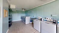 Located at 119 Sanders Ferry Road in Hendersonville, Tennessee, this shared laundry facility offers a clean, functional, and welcoming environment for its users. The single-room space is defined by its distinctive soft blue beadboard wall paneling, which lends a classic, cottage-like character to the interior. White crown molding provides a crisp finishing detail that ties the room together.

The laundry room is equipped with multiple front-loading and top-loading washers and dryers, arranged efficiently along the walls to maximize usable floor space. A centrally located utility sink adds practical convenience for pre-treating garments. A mounted garment rod along one wall provides a dedicated area for hanging freshly laundered clothing.

Natural light fills the space through a large, multi-pane window that frames a pleasant view of the surrounding greenery — creating a bright and airy atmosphere. A ceiling fan helps maintain comfortable air circulation throughout. Durable tile flooring covers the entire room, offering easy maintenance suited to the demands of a high-use facility.

A bulletin board near the entrance door serves as an informational hub for users, and a fire extinguisher is conveniently mounted nearby for safety. Overall, this laundry facility combines practicality with a tidy, well-maintained aesthetic, making it a reliable and comfortable shared amenity.