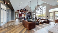 Located at 1070 59th Ave in Kenosha, Wisconsin, this single-story community clubhouse is a well-appointed social hub designed for gathering, recreation, and relaxation. The main lounge area commands attention with dramatic vaulted ceilings and floor-to-ceiling windows that flood the space with natural light and provide sweeping views of the outdoor amenity deck, complete with patio seating and a pool area beyond. Warm hardwood-style flooring runs throughout, anchoring a bold interior design that blends rustic and contemporary elements.

A striking red plaid accent wall serves as a focal point in the central lounge, adorned with framed artwork and neon signage, while statement chandeliers and globe pendant lighting add a refined industrial touch. Plush leather seating arrangements create comfortable conversation zones throughout.

The game room features a full-size billiards table beneath a circular chandelier, with additional high-top seating nearby. A well-equipped kitchen showcases natural wood cabinetry, black matte appliances, a bold red island with bar seating, dramatic tile backsplash, and Edison-bulb pendant lighting.

A secondary lounge offers a large flat-screen TV, oversized board games, and casual leather seating. The corridors lead to a fitness center with strength and cardio equipment, and decorative touches including firewood displays and curated wall art make every transition space feel intentional and inviting.