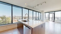 Located in San Diego's vibrant East Village neighborhood, this high-rise unit at 310 A St offers a contemporary urban living experience defined by modern design and sweeping city views. The open-concept living and kitchen area is anchored by expansive floor-to-ceiling windows framed in sleek black, flooding the space with natural light while showcasing panoramic views of the San Diego skyline and surrounding cityscape. Light wood-tone flooring runs throughout the main living areas, complementing the clean, neutral palette.

The kitchen is thoughtfully designed with rich dark wood cabinetry, light quartz countertops, and a full suite of stainless steel appliances, including a refrigerator, electric range, microwave, and dishwasher. A central island with an undermount sink and industrial-style faucet serves as a functional focal point. Track lighting overhead enhances the modern aesthetic.

The bedrooms feature plush carpeting and large windows that continue the theme of abundant natural light and elevated city views. The primary bathroom includes a double-sink vanity with dark wood cabinetry, large-format tile flooring, and a glass-enclosed shower. A secondary bathroom offers a tub-shower combination with marble-style tile surround. The overall ambiance is clean, contemporary, and well-appointed.