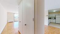 This single-floor unit offers a clean, functional layout with a consistent design language throughout. The most striking flooring feature is the warm parquet wood pattern that extends across the living areas and bedrooms, adding a classic, timeless character to the space.

The living area is generously proportioned, filled with natural light, and anchored by floor-to-ceiling sliding glass doors that open directly onto a private balcony with open views of the surrounding urban landscape. This seamless indoor-outdoor connection makes the living space feel bright and airy.

The kitchen is efficiently designed in an L-shaped configuration, featuring white cabinetry with brushed nickel hardware, dark laminate countertops, and white appliances including a gas range, dishwasher, refrigerator, and microwave. Light tile flooring keeps the kitchen feeling clean and practical.

The bedroom is a well-proportioned, quiet room with the same warm parquet flooring and a window that draws in natural light. Storage is well-addressed with full-height closet doors located near the entry, providing ample organizational space.

The bathroom includes a full tub-shower combination with a curtain rod, tile surround, and warm-toned walls, complemented by a vanity with granite-style countertop. The overall palette of the unit — whites, creams, and natural wood tones — creates a cohesive and inviting atmosphere throughout.