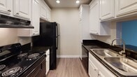 Located at 1919 E Birch St in Brea, California, this single-floor unit offers a well-organized layout designed for comfortable living. The main living area features dark hardwood-style flooring that extends throughout, complemented by neutral warm-toned walls and a textured ceiling. Structural beam details add architectural character to the space. A sliding glass door opens directly to a private patio, allowing natural light to fill the room and providing easy access to outdoor greenery.

The living area flows openly into a dining space, which connects to the galley-style kitchen via a pass-through counter. The kitchen is well-appointed with crisp white cabinetry, dark granite countertops, black appliances including a refrigerator and range, a stainless steel sink, and recessed lighting overhead. Light wood-style flooring grounds the kitchen's clean, contrasting aesthetic.

The bedroom is carpeted for comfort and features a large window fitted with vertical blinds, inviting ample natural light and views of the surrounding landscape. The bathroom includes a full tub-shower combination with brushed nickel fixtures, wood-style flooring, and a vanity with dark countertop detailing. A ceiling fan in the dining area and vertical blinds throughout complete the functional and cohesive design of this Brea residence.