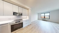 Located at 202 Fourth Ave in Asbury Park, NJ, this thoughtfully designed one-bedroom, one-bathroom residence offers a clean, modern aesthetic throughout its efficiently organized single-floor layout. Light wood-tone flooring flows seamlessly across the entire space, creating a warm and cohesive feel.

The open-concept living area combines the kitchen, dining, and living spaces into one bright, airy zone. The contemporary kitchen is outfitted with sleek white flat-panel cabinetry extending to the ceiling for maximum storage, stainless steel appliances including a French door refrigerator, electric range with over-the-range microwave, and dishwasher, complemented by white quartz countertops and a textured tile backsplash. Track lighting overhead adds a modern touch and illuminates the kitchen efficiently.

The living area benefits from a large black-framed window that invites natural light and frames views of the Asbury Park streetscape. The spacious bedroom features its own oversized window with multi-pane black framing, a ceiling fan, and a wall-mounted HVAC unit. Two closets provide ample storage throughout the unit. Additional conveniences include an in-unit laundry area and a utility room. The overall ambiance is bright, clean, and contemporary, well-suited for modern urban living.