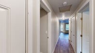 This single-floor, 1-bedroom, 2-bathroom residence offers a practical and comfortable layout designed to maximize its efficient footprint. A central hallway with durable hardwood-style flooring connects the main living areas, featuring overhead lighting and attic access, setting a clean and organized tone throughout.

The living room is a generously proportioned open space finished with rich, dark hardwood-style plank flooring and neutral-toned walls, creating a warm and versatile environment suited to a variety of furnishing arrangements. Natural light filters in through a window at the far end, enhancing the room's airy feel.

The bedroom is well-sized, finished with plush wall-to-wall carpeting and neutral walls that contribute to a calm, restful atmosphere. A wide sliding double-door closet provides substantial storage, while a window with blinds overlooks greenery outside, bringing in natural light and a connection to the outdoors. A baseboard heater ensures comfort year-round.

Both bathrooms are finished consistently with wood-style flooring, white vanities with undermount sinks, large mirrors, and full tub-shower combinations with brushed nickel fixtures, offering clean and functional spaces. The cohesive design throughout the unit, combining neutral tones with practical finishes, creates a welcoming and move-in ready home.