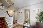 Located at 50 Irving Street in Cambridge, MA, this multi-floor property spans three levels, offering a well-organized layout with a generous main floor and two additional floors above and below. The main level makes an immediate impression with a sweeping curved staircase finished with a rich mahogany banister, white spindles, and a bold patterned stair runner. The entryway is bright and welcoming, featuring soft gray walls, warm recessed lighting, wall sconces, and an ornate full-length mirror that adds depth to the space. Warm hardwood floors run through multiple rooms, complementing the light-toned palette throughout. The bedrooms are comfortably sized, bathed in natural light from large windows, and include ample storage. One bedroom opens directly to a private balcony with French doors, offering outdoor views of the surrounding neighborhood. The kitchenettes are distinctly designed — one features crisp white cabinetry with a sleek induction cooktop and stainless steel sink, while another showcases bold green cabinetry with a classic white subway tile backsplash and a gas cooktop. The bathroom is finished with an elegant arabesque marble tile floor, a bright window, and clean white fixtures. Throughout, the space blends classic architectural character with modern, functional updates.