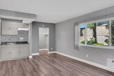 Located at 2630 W Lincoln Ave in Anaheim, California, this single-floor unit offers an efficient and thoughtfully arranged layout. The main living area is finished with smooth, wood-style laminate flooring in a warm grey-brown tone that runs throughout, complementing the light grey walls and white baseboards for a clean, modern aesthetic. A textured ceiling adds subtle visual character overhead.

Natural light enters through a large sliding window fitted with sheer curtains, offering views of greenery outside and creating a bright, welcoming atmosphere. A wall-mounted HVAC unit provides climate control directly within the living space.

A built-in kitchenette is tucked into one corner of the main room, featuring upper cabinetry, a compact sink with lower cabinet storage, and a countertop workspace — all finished in a consistent grey and wood-tone palette that ties seamlessly into the overall design.

A dedicated walk-in closet accessible from the main living area provides practical storage space with an open rod system visible from the entrance.

The bathroom is finished with beige ceramic tile flooring and full tile surround in the tub/shower area. It includes a standard toilet, a towel bar, and a bathtub, offering functional amenities in a compact, well-maintained space. This unit is ideally suited for individuals seeking a manageable, low-maintenance living space in Anaheim.