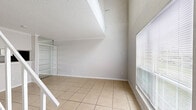 Located at 10301 Sandpiper Dr in Houston, TX, this two-story home offers a thoughtful layout spread across two floors. The main level features light-filled living spaces with neutral-toned tile flooring, an open living room anchored by a white-railed staircase, and a dedicated entrance. Natural light filters through slatted window blinds, lending a bright, airy feel to the common areas. The galley-style kitchen is efficiently designed with white cabinetry, dark granite-look countertops, a double sink, and black appliances including a refrigerator, range, and dishwasher — all complemented by matching tile flooring and a pantry for additional storage. The upper level is home to the generously sized primary bedroom, finished with plush carpet, a ceiling fan, and a window for natural light. The open loft-style layout of the upper floor adds a sense of openness, with a white railing overlooking the level below. Three bathrooms serve the home, including one featuring a tiled tub-and-shower combination with decorative diamond-tile accents. Additional highlights include two closets, textured ceilings throughout, and a clean, neutral color palette that creates a cohesive and move-in-ready atmosphere.