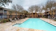 Situated at 111 Edie Ann Dr in Lafayette, Louisiana, this single-story property offers a welcoming community environment defined by classic brick construction and lush, established landscaping. The standout feature of the outdoor space is a generously sized swimming pool with clear, blue water set atop an elegant stone paver deck. Multiple lounge chairs are positioned along the poolside, providing ample space for relaxation and recreation. The pool area is enclosed by a sturdy wrought iron fence, ensuring both security and an open visual aesthetic. Mature deciduous trees frame the perimeter, offering natural shade and a sense of seclusion. A covered pavilion structure with a pitched roof is visible in the background, complementing the brick exterior of the surrounding buildings and suggesting a dedicated area for outdoor gathering. Picnic tables nearby further enhance the social amenities of the space. The overall ambiance is that of a well-maintained, community-oriented property that balances functional outdoor living with classic Southern architectural character, making it an inviting setting for residents and visitors alike.
