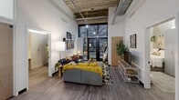 Located at 619 E University Ave in Ann Arbor, MI, this 4-bedroom, 2-bathroom unit offers a distinctive industrial-modern aesthetic across a single floor. Soaring ceilings with exposed ductwork, concrete elements, and hardwood-style flooring set a striking architectural tone throughout. The open-concept living, dining, and kitchen area serves as the heart of the unit, anchored by large floor-to-ceiling windows that bring in natural light and outdoor views. The kitchen features stainless steel appliances, two-tone cabinetry with bold accent uppers, dark granite countertops, and a breakfast bar with barstool seating — ideal for both cooking and casual dining. The living area accommodates generous seating and benefits from the dramatic ceiling height. Both bathrooms are finished with clean, modern fixtures, wood-toned floating vanities, white countertops, and glass-enclosed walk-in showers. The four bedrooms provide private accommodations, including a compact but functional primary bedroom. A dedicated in-unit laundry room includes a full-size washer and dryer. One closet provides additional storage. The overall ambiance blends urban industrial character with contemporary finishes, making this a well-equipped and visually dynamic space.