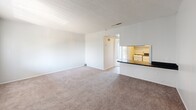 Located in Largo, Florida, this one-bedroom, one-bathroom unit offers a well-organized, single-floor layout that makes efficient use of its compact footprint. The living room is bright and open, featuring plush wall-to-wall carpeting, neutral-toned walls, and a textured ceiling. A pass-through counter connects the living area to the kitchen, which includes dark countertops and white cabinetry, enhancing the sense of openness between the two spaces. Natural light filters in through vertical blinds on the windows. The bedroom is a comfortable, carpeted retreat with a sliding glass door that opens onto a private balcony, offering pleasant outdoor views of mature trees and what appears to be a waterfront setting — a standout feature of this unit. The balcony provides a tranquil outdoor extension of the living space. A closet is accessible directly from the bedroom. The bathroom is clean and functional, featuring wood-look vinyl flooring, a tub-shower combo, a toilet, and a vanity with a dark speckled countertop. The entry area transitions from hardwood-style flooring into the carpeted main living space, adding a subtle design detail at the threshold. Overall, the unit offers a bright, neutral palette suited for comfortable everyday living.