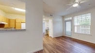 This single-floor unit is characterized by warm wood-style plank flooring that extends consistently throughout all living areas, bedrooms, and bathrooms, creating a cohesive and welcoming aesthetic. The open layout connects a hallway entry to a spacious living and dining area, with natural light filtering in through multiple windows dressed with horizontal blinds. Crown molding accents the main living area, adding a refined detail to the otherwise clean, neutral design.

The kitchen features warm-toned wood cabinetry, granite countertops, a stainless steel sink with a pull-down faucet, and a pass-through window that opens to the dining area, promoting an open, connected feel. Built-in shelving and ample cabinetry provide generous storage.

The bedrooms are well-proportioned, each with ceiling fans, closet access, and windows that allow natural light. The unit includes two bathrooms: one with a granite-topped vanity, wood cabinetry, and a tiled shower-tub combination, and a second fully accessible bathroom equipped with a roll-in shower, fold-down shower seat, grab bars, and a separate handheld showerhead, catering to diverse accessibility needs.