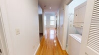 Located at 230 North 6th in downtown Richmond, VA, this one-bedroom, one-bathroom residence offers a well-organized layout designed for comfortable urban living. The open-concept kitchen and living area forms the heart of the unit, featuring warm hardwood floors that reflect natural light from large windows. The kitchen is outfitted with light maple cabinetry, dark countertops, a classic subway tile backsplash, and a full suite of stainless steel appliances including a refrigerator, electric range, built-in microwave, and dishwasher — providing both style and functionality. The spacious bedroom is finished with plush wall-to-wall carpeting and connects to a generous walk-in closet equipped with wire shelving and hanging rods along two walls, offering ample storage. A hallway links the main living area to the private quarters, maintaining a clear separation of spaces. The bathroom features a full soaking tub and shower surrounded by white subway tile, complemented by tile flooring and warm wood vanity accents. Recessed lighting throughout the living area and clean, neutral-toned walls create a bright, modern ambiance that suits a variety of interior styles.