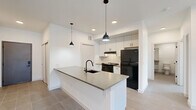 Located at 359 E Rio Grande St in Colorado Springs, CO, this thoughtfully designed 2-bedroom, 1-bathroom residence offers a clean, modern aesthetic across a single floor. The open-concept living and kitchen area serves as the heart of the home, featuring large-format tile flooring, recessed lighting, and stylish black pendant lights. The kitchen is equipped with a spacious island with a built-in sink and matte black faucet, sleek gray countertops, white cabinetry, a tile backsplash, and black appliances including a range and refrigerator. The living room extends to a private balcony through sliding glass doors, complemented by a ceiling fan and a wall-mounted mini-split HVAC unit. Both bedrooms are carpeted and bright, with one featuring a window and its own mini-split unit. The full bathroom showcases striking floor-to-ceiling dark tile in the walk-in shower, a floating vanity, pendant lighting, and an accessible layout with grab bars. A dedicated laundry room houses a full-size washer and dryer. Three closets provide ample storage throughout the unit.