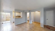 Located at 5720 S Alameda St, Unit 103 in Corpus Christi, Texas, this single-floor unit features a clean, functional layout with consistent tile flooring throughout the living spaces. The open main living area is finished in soft blue-gray tones with crisp white trim, creating a light and airy atmosphere. A pass-through window connects the kitchen to the living area, adding an open feel and providing a convenient breakfast bar counter. The kitchen is equipped with white cabinetry, a tile backsplash, white appliances including an electric range and refrigerator, and a single-basin sink. Natural light filters into the kitchen and living areas via a sliding glass door that opens to an outdoor space. Additional rooms branch off the main living area, offering flexible use of space, with one room featuring a wall-unit air conditioner and a window with blinds. A bathroom with a vanity and cabinetry is also accessible from the central corridor. The layout is efficiently arranged, with arched and squared doorways guiding the flow between spaces. Overall, the unit presents a straightforward, well-maintained interior suited for comfortable everyday living in the Corpus Christi area.