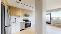 Located at 331 Metcalfe St in the heart of Ottawa, this well-appointed 2-bedroom, 2-bathroom unit offers a clean, modern aesthetic throughout. Light-toned hardwood flooring flows seamlessly across the living areas and bedrooms, lending a bright and cohesive feel to the space.

The open kitchen is a standout feature, finished with two-tone cabinetry — warm natural wood uppers paired with crisp white lower cabinets — complemented by light stone countertops and a white tile backsplash. Stainless steel appliances, including a full-size refrigerator, electric range, over-the-range microwave, and dishwasher, complete the functional and stylish cooking space. A sleek track lighting fixture adds a contemporary touch overhead.

The living room is generously proportioned and bathed in natural light. Both bedrooms are well-sized, with the primary bedroom offering a comfortable footprint. Large windows throughout the unit frame elevated views of the Ottawa cityscape and surrounding neighbourhood, flooding each room with natural light.

The two bathrooms are clean and modern, featuring wood-accented vanities with black hardware, mirrors, and a full tub-shower combination. A central hallway connects all rooms efficiently, contributing to a logical and practical layout. The overall ambiance is bright, neutral, and move-in ready.