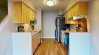 This thoughtfully designed two-story residence in Dexter, Michigan offers two bedrooms and one and a half bathrooms with premium upgrades throughout. The galley-style kitchen is well-appointed with warm honey-toned cabinetry, light stone countertops, and a full suite of stainless steel appliances including a refrigerator, dishwasher, and range with overhead ventilation. A stacked washer and dryer unit is conveniently integrated within the kitchen area, adding practical in-unit laundry access. The kitchen flows into an open area with durable hardwood-style flooring that extends through the main living spaces, lending a clean, contemporary feel. The bedrooms are generously sized and carpeted for comfort, each featuring large sliding windows that bring in ample natural light and views of the surrounding neighborhood. The primary bedroom includes ceiling fan lighting and direct access to a walk-in closet. The full bathroom features light wood cabinetry, a white countertop vanity, tile flooring, and brushed nickel fixtures and grab bars. A half bath provides additional convenience. Throughout the home, neutral tones, white trim, and consistent finishes create a cohesive and inviting atmosphere well-suited for comfortable everyday living.