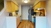 This thoughtfully designed two-story residence in Dexter, Michigan offers two bedrooms and one and a half bathrooms with premium upgrades throughout. The galley-style kitchen is well-appointed with warm honey-toned cabinetry, light stone countertops, and a full suite of stainless steel appliances including a refrigerator, dishwasher, and range with overhead ventilation. A stacked washer and dryer unit is conveniently integrated within the kitchen area, adding practical in-unit laundry access. The kitchen flows into an open area with durable hardwood-style flooring that extends through the main living spaces, lending a clean, contemporary feel. The bedrooms are generously sized and carpeted for comfort, each featuring large sliding windows that bring in ample natural light and views of the surrounding neighborhood. The primary bedroom includes ceiling fan lighting and direct access to a walk-in closet. The full bathroom features light wood cabinetry, a white countertop vanity, tile flooring, and brushed nickel fixtures and grab bars. A half bath provides additional convenience. Throughout the home, neutral tones, white trim, and consistent finishes create a cohesive and inviting atmosphere well-suited for comfortable everyday living.