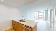 Located at 955 Eleventh Avenue in San Diego, CA, this modern one-bedroom, one-bathroom residence offers a thoughtfully designed open-concept layout with clean lines and contemporary finishes. Light wood-tone flooring flows seamlessly throughout the space, complementing the crisp white walls and creating a bright, cohesive aesthetic.

The living area is anchored by dramatic floor-to-ceiling windows that frame sweeping views of the San Diego skyline, flooding the space with natural light. A private balcony extends the living area outdoors, offering a perfect vantage point over the city.

The kitchen is a standout feature, centered around a sleek island with a white quartz countertop, an undermount sink, and warm wood cabinetry. Stainless steel appliances — including a refrigerator, range, microwave, and dishwasher — complete the modern culinary setup. Recessed lighting adds a polished finish overhead.

The bedroom is a calm retreat with neutral tones, continued light wood flooring, and a mirrored sliding-door closet that enhances the sense of space. The bathroom features large-format tile flooring, a soaking tub with marble-style tile surround, a wood-cabinet vanity with a mirror, and clean, modern fixtures throughout.