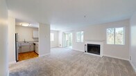 This single-floor, 3-bedroom, 2-bathroom home offers a practical and well-organized layout designed for comfortable living. The open-concept living room serves as the heart of the space, featuring plush carpeting, neutral walls, and a classic wood-burning fireplace framed by a white tile surround and mantel. Multiple windows with blinds allow natural light to fill the room, while sliding glass doors provide access to an outdoor area. The kitchen is positioned adjacent to the living room and is separated by a half-wall pass-through counter, creating an efficient, connected feel. It is equipped with stainless steel appliances, including a refrigerator and electric range, white cabinetry, and hardwood flooring. The three bedrooms are carpeted and feature neutral tones, individual windows for natural light, and baseboard heating units. At least one bedroom includes a closet with built-in shelving. The two bathrooms are finished with light wood-tone vanities, single-basin sinks, and clean white fixtures. One bathroom features a walk-in shower, while the other includes a full tub-shower combination. A hallway connects the private areas of the home, completing this efficiently designed single-level residence.