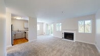 This single-floor, 3-bedroom, 2-bathroom home offers a practical and well-organized layout designed for comfortable living. The open-concept living room serves as the heart of the space, featuring plush carpeting, neutral walls, and a classic wood-burning fireplace framed by a white tile surround and mantel. Multiple windows with blinds allow natural light to fill the room, while sliding glass doors provide access to an outdoor area. The kitchen is positioned adjacent to the living room and is separated by a half-wall pass-through counter, creating an efficient, connected feel. It is equipped with stainless steel appliances, including a refrigerator and electric range, white cabinetry, and hardwood flooring. The three bedrooms are carpeted and feature neutral tones, individual windows for natural light, and baseboard heating units. At least one bedroom includes a closet with built-in shelving. The two bathrooms are finished with light wood-tone vanities, single-basin sinks, and clean white fixtures. One bathroom features a walk-in shower, while the other includes a full tub-shower combination. A hallway connects the private areas of the home, completing this efficiently designed single-level residence.