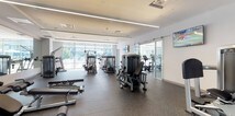 This fitness center is a spacious, modern facility designed to accommodate a comprehensive range of workout routines. The space is organized across distinct zones, separated by sleek glass sliding doors that allow for visual openness while defining separate areas for different training activities. The flooring throughout is durable rubberized speckled material, well-suited for heavy equipment and high-traffic use.

The strength training area features a Life Fitness cable machine and a multi-functional rack with an adjustable bench, flanked by floor-to-ceiling mirrors that enhance the sense of space. A dedicated free weights section includes a full dumbbell rack with an extensive range of weights, positioned alongside mirrored walls for form monitoring. Additional selectorized machines provide options for targeted muscle group training.

The cardio zone, visible through the glass partition, houses treadmills, ellipticals, and upright bikes, with wall-mounted flat-screen TVs for entertainment during workouts. Large floor-to-ceiling windows along one wall bring in ample natural light and offer views of the surrounding outdoor environment. Recessed and linear pendant lighting ensures the space remains well-lit throughout. The overall atmosphere is clean, bright, and professionally appointed.