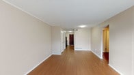 This single-floor, one-bedroom, one-bathroom unit offers a practical and well-organized layout designed to maximize its cozy footprint. The living area is immediately welcoming, showcasing warm hardwood-style flooring that extends throughout the main spaces, complemented by neutral beige walls and crisp white baseboards and crown molding. A textured ceiling adds subtle character, while floor vents indicate a central HVAC system for year-round climate control. Natural light filters in through windows, brightening the open feel of the main living space.

The kitchen is positioned near the entryway and features white cabinetry with ample upper and lower storage, white countertops, and black appliances including a range on each side. The dark wood six-panel entry door adds a bold contrast to the otherwise light interior palette.

The bedroom is carpeted in a neutral tan tone, providing comfort underfoot, and includes a window that allows in natural light. Crown molding carries through this room as well, maintaining a consistent, tidy aesthetic.

The bathroom is clean and straightforward, featuring a full tub and shower combination with white tile surround and chrome fixtures, paired with warm beige walls that echo the unit's overall color scheme.