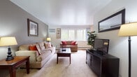 This updated two-bedroom, one-bathroom residence is thoughtfully laid out across a single floor, offering a well-organized and functional living environment. The living room serves as the centerpiece of the home, featuring neutral-toned carpet, soft neutral wall colors, and a large picture window that draws in natural light and offers views of surrounding greenery. The room comfortably accommodates multiple seating areas, creating a welcoming and versatile space.

The galley-style kitchen runs parallel along two walls, providing ample upper and lower cabinetry in warm wood tones alongside a white gas range, refrigerator, and a double sink with a clean white countertop. The adjacent dining area features a ceiling fan and a window with vertical blinds, adding to the room's natural brightness.

Both bedrooms are carpeted and well-proportioned, each offering a window with outdoor views and sufficient space for standard furnishings. The shared full bathroom includes a single-sink vanity with wood cabinetry, a tiled tub-shower combination, and tile flooring. Neutral tones throughout the home create a cohesive, move-in-ready aesthetic well-suited to comfortable everyday living.
