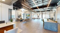 Located at Bradford Drive NW in Huntsville, Alabama, this expansive single-floor amenity space presents a sophisticated blend of industrial and contemporary design. The open-plan layout spans a generous footprint, unified by large-format tile flooring and soaring exposed ceilings fitted with dark-painted ductwork, structural beams, and sleek linear LED lighting that casts a warm, even glow throughout.

A striking stone-clad fireplace column serves as the architectural centerpiece, anchoring a well-appointed lounge area furnished with tufted sofas, accent chairs, and curated artwork. Adjacent to the main lounge, a dedicated seating zone with floor-to-ceiling windows offers abundant natural light and direct views to an outdoor terrace, creating a seamless indoor-outdoor connection.

A prominent reception desk with a wood-paneled base and white quartz surface is positioned near the entry, complemented by statement pendant lighting above. Glass-partitioned private offices or conference rooms line one side of the space, providing functional separation without sacrificing the open feel. A game area features a full-length shuffleboard table bathed in natural light from expansive window walls. A herringbone wood accent wall and a bar-height counter with green velvet seating add further warmth and character throughout this well-designed communal space.
