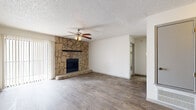 This single-story, 2-bedroom, 4-bathroom home offers a well-organized layout with a variety of functional spaces, including a living room, kitchen, hallway, utility room, and two closets. The living room is a standout area, anchored by a dramatic floor-to-ceiling natural stone fireplace that serves as a striking focal point. Wood-look flooring runs throughout the main living areas, and a ceiling fan with light fixture adds both style and practicality. A sliding door provides access to the exterior, allowing natural light to fill the room. The kitchen features cabinetry in a neutral tone, tile backsplash, and a pass-through window with a built-in counter that opens to a dining or flex area flanked by open shelving — ideal for storage or display. The primary bedroom is generously sized, finished with wood-look flooring, a ceiling fan, and direct access to a bathroom featuring a wide vanity with white quartz countertops and ample cabinet storage. The secondary bedroom is carpeted and brightened by a window with blinds, also equipped with a ceiling fan. Both walk-in closets offer built-in shelving and hanging rods. The bathrooms maintain a consistent, clean aesthetic with updated vanities and wood-look flooring throughout.