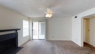 This single-floor residence offers a clean and functional layout designed for comfortable everyday living. The main living area is finished with wall-to-wall carpeting that adds warmth underfoot, while neutral-toned walls provide a versatile backdrop suitable for a variety of interior styles. A ceiling fan with an integrated light fixture is centrally mounted, offering both ambient lighting and air circulation throughout the room. Natural light fills the space through a large sliding glass door fitted with vertical blinds, which leads directly to an outdoor area — ideal for enjoying fresh air or additional outdoor living. A side window further enhances the brightness of the room, contributing to an airy and open atmosphere. The textured ceiling adds a classic residential character to the space. The overall design is practical and straightforward, with a neutral palette that makes it easy to personalize. The seamless flow between the interior and the outdoor access point gives the living area a sense of openness that extends beyond its walls, making the space feel welcoming and well-connected to its surroundings.