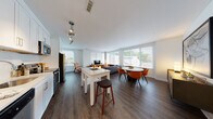 This well-appointed two-bedroom, two-bathroom residence is designed with a contemporary open-concept layout that seamlessly connects the kitchen, dining, and living areas. Rich dark hardwood flooring runs throughout the main living space, complementing the crisp white walls and clean-lined finishes that define the home's modern aesthetic.

The kitchen is outfitted with stainless steel appliances—including a refrigerator, range, microwave, and dishwasher—paired with white shaker cabinetry, light countertops, and a subway tile backsplash. Track lighting overhead adds a functional and stylish touch. A white kitchen island with bar seating bridges the kitchen and dining area.

The living room is a bright, airy space anchored by large windows fitted with white horizontal blinds, offering generous outdoor views and an abundance of natural light. A structural concrete column adds an industrial design accent to the corner of the room.

Both bedrooms are comfortably sized with carpet flooring, large windows, and soft neutral tones that create a calm, restful atmosphere. Each bedroom is served by its own bathroom: one features a tiled tub-shower combination with a white vanity, while the second offers a walk-in shower with tile surround and an equally clean, modern finish.
