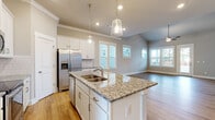 Located in Opelika, Alabama, this single-story home offers a thoughtfully designed layout across four bedrooms and two bathrooms. The open-concept kitchen and living area serves as the heart of the home, highlighted by a central granite-topped island with a built-in sink and pendant lighting overhead. White shaker-style cabinetry, a classic subway tile backsplash, and stainless steel appliances — including a French door refrigerator, electric range, and built-in microwave — complete the kitchen. Light hardwood flooring flows throughout the main living areas, complemented by neutral gray walls and crown molding that lend a clean, polished aesthetic. Multiple windows allow natural light to fill the space. The bedrooms are carpeted and bright, each featuring windows that invite natural light. The primary bedroom offers a comfortable footprint with an adjoining walk-in closet equipped with wire shelving. The bathrooms include a tub-shower combination with a smooth surround. A dedicated laundry room houses a full-size washer and dryer. The attached garage features a concrete floor and an automatic opener, providing convenient covered parking and additional storage.