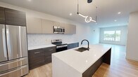 This thoughtfully designed one-bedroom, one-bathroom unit in West Lafayette, Indiana offers a modern aesthetic with high-quality finishes throughout. The open-concept layout seamlessly connects the kitchen and living area, maximizing the efficient use of space. The kitchen is a standout feature, showcasing two-tone cabinetry with dark lower cabinets and warm taupe uppers, a white subway tile backsplash, stainless steel appliances including a refrigerator, electric range, and microwave, and a large quartz waterfall island with an undermount sink and matte black faucet. A contemporary pendant light fixture adds a stylish focal point above the island. Light hardwood flooring flows throughout the main living areas, complementing the clean white walls and recessed lighting. The bedroom is a bright, comfortable retreat featuring a wide window with outdoor views and a double-door closet with modern panel detailing and matte black hardware. The bathroom is finished with large-format tile flooring, a sleek white vanity with black hardware, a framed mirror, and a dark marble-tiled shower. A dedicated in-unit laundry area houses a full-size Whirlpool washer and dryer, adding everyday convenience to this well-appointed West Lafayette residence.