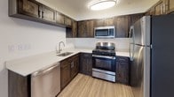 This single-floor unit offers a thoughtfully designed layout that balances comfort and functionality throughout. The open-concept living area is finished with wood-look vinyl flooring and features a ceiling fan with light fixture, creating a bright and airy atmosphere. Sliding glass doors invite natural light and provide access to the outdoors. The kitchen flows seamlessly from the living space and is outfitted with rich dark wood cabinetry, white countertops, and a full suite of stainless steel appliances including a refrigerator, gas range, microwave, and dishwasher. An entry closet near the front door adds practical storage.

The bedrooms are carpeted for warmth and comfort, each with windows dressed in horizontal blinds that allow for adjustable natural light. The rooms offer clean, neutral walls that provide a versatile backdrop for any furnishing style.

The bathrooms are finished with wood-look flooring and dark wood vanities topped with light countertops. One bathroom is notably accessible, featuring stainless steel grab bars positioned throughout, a roll-in shower area, and an elongated vanity with ample drawer storage, making the space both functional and inclusive. Overall, the unit presents a clean, modern aesthetic with consistent finishes across all spaces.