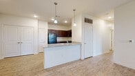 This single-story residence is designed with a clean, contemporary aesthetic throughout. The kitchen serves as a central feature, equipped with rich dark wood cabinetry, granite-style countertops, and a full suite of black appliances including a refrigerator, range, and microwave. A peninsula with an integrated sink extends into the adjacent living area, creating an open, connected layout ideal for everyday living. Light wood-look flooring runs consistently through the main living spaces, complementing the neutral white walls and adding warmth to the interior.

The living and dining areas benefit from natural light through blinded windows and sliding glass door access to the exterior, with ceiling fans providing additional comfort. Bedrooms are finished with plush carpet and offer generous closet space, including walk-in style storage in at least one room. Multiple windows allow natural light to fill the carpeted bedrooms, enhancing the sense of openness.

Two full bathrooms feature the same wood-look flooring, dark vanity cabinetry, white countertops, and tiled tub-shower combinations. The overall design is cohesive and functional, with a neutral palette and practical finishes throughout.