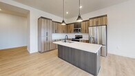 Located in Holladay, Utah, this contemporary 2-bedroom, 2-bathroom residence offers a well-designed single-floor layout with modern finishes throughout. The open-concept kitchen and living area serves as the heart of the home, featuring wood-grain cabinetry, white quartz countertops, a central island with an undermount sink and pendant lighting, and stainless steel appliances. Light hardwood-style flooring runs through the main living areas, enhancing the bright, airy atmosphere. Large windows and a wall of sliding glass doors flood the space with natural light and open to a tiled balcony with sweeping views of the Wasatch Mountains. The generously sized primary bedroom includes an elegant tray ceiling with a ceiling fan, plush carpet, a spacious sliding-door closet, and corner windows framing picturesque mountain scenery. The second bedroom also features hardwood-style flooring, a ceiling fan, and its own mountain views. Both bathrooms are finished with light wood vanities, white subway tile tub-surround enclosures, and matte black hardware and fixtures. Hallways connect the layout efficiently, and the overall design balances clean, minimalist aesthetics with warm, natural materials throughout.