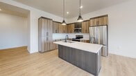 Located in Holladay, Utah, this contemporary 2-bedroom, 2-bathroom residence offers a well-designed single-floor layout with modern finishes throughout. The open-concept kitchen and living area serves as the heart of the home, featuring wood-grain cabinetry, white quartz countertops, a central island with an undermount sink and pendant lighting, and stainless steel appliances. Light hardwood-style flooring runs through the main living areas, enhancing the bright, airy atmosphere. Large windows and a wall of sliding glass doors flood the space with natural light and open to a tiled balcony with sweeping views of the Wasatch Mountains. The generously sized primary bedroom includes an elegant tray ceiling with a ceiling fan, plush carpet, a spacious sliding-door closet, and corner windows framing picturesque mountain scenery. The second bedroom also features hardwood-style flooring, a ceiling fan, and its own mountain views. Both bathrooms are finished with light wood vanities, white subway tile tub-surround enclosures, and matte black hardware and fixtures. Hallways connect the layout efficiently, and the overall design balances clean, minimalist aesthetics with warm, natural materials throughout.