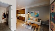 Located at 372 Fourth Ave in San Diego's dynamic Bankers Hill neighborhood, this single-floor unit blends modern design with bohemian character throughout its thoughtfully arranged layout. The open-concept living and kitchen area serves as the heart of the space, where a comfortable white sofa and rattan coffee tables sit beneath colorful surf-themed wall art, setting a relaxed coastal tone. Polished concrete floors extend seamlessly throughout, lending an industrial-chic aesthetic that ties each area together. The kitchen is well-appointed with rich walnut-toned cabinetry, white subway tile backsplash, stainless steel appliances — including a French door refrigerator, range, microwave, and dishwasher — and ample counter space for meal preparation. A dining area with warm wood accents provides an inviting space for everyday meals. The bedroom is a serene retreat, highlighted by a striking macramé wall hanging, soft ambient lighting, and a sliding closet with built-in storage organization. Vibrant framed textile art adds a global, artisan touch. The bathroom features a clean, contemporary design with a wood-faced vanity, white quartz countertop, large mirror, and a tiled shower-tub combination, completing this well-curated urban San Diego residence.