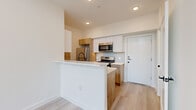 This modern residence in Austin, TX offers a thoughtfully designed layout across a single floor, complemented by dramatic double-height ceilings that create an impressive sense of volume and openness. Light wood-look flooring runs throughout, tying the spaces together with a clean, cohesive aesthetic.

The open-concept kitchen features a peninsula with a white quartz countertop and a built-in sink, warm wood cabinetry paired with crisp white upper cabinets, subway tile backsplash, and a full suite of stainless steel appliances including a refrigerator, range, and over-the-range microwave. The living area benefits from floor-to-ceiling windows and a glass-paned entry door that invite abundant natural light and views of surrounding greenery.

A striking black steel staircase with horizontal railings serves as an architectural focal point, ascending alongside the soaring two-story wall. In-unit washer and dryer connections are conveniently accessible from the hallway.

The bedroom is well-proportioned, fitted with a ceiling fan, windows framing leafy outdoor views, and a dedicated closet. The full bathroom is elegantly finished with large-format tile, a floating wood vanity with white countertop, a glass-enclosed shower, a soaking tub, and matte black fixtures. A second half-bath echoes the same warm wood vanity and clean white palette.