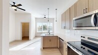 Located at 2220 Berryhill Road in Charlotte, NC, this thoughtfully designed single-floor unit makes efficient use of its space through a clean, modern aesthetic and an open-concept layout. The combined living, dining, and kitchen area serves as the heart of the unit, characterized by soaring ceilings and abundant natural light streaming through large windows. Light wood-tone luxury vinyl plank flooring runs throughout, complementing the bright white walls and lending a warm, cohesive feel.

The kitchen is well-appointed with light natural wood cabinetry, white subway tile backsplash, quartz countertops, and a full suite of stainless steel appliances including a range, microwave, dishwasher, and refrigerator. A peninsula with an undermount sink and pendant lighting above adds both functionality and visual appeal, flowing seamlessly into the dining and living areas. Ceiling fans in the main living space enhance comfort throughout.

The bathroom features a wood-toned vanity with quartz countertop, undermount sink, black hardware accents, and a full soaking tub with shower. Additional practical spaces include a pantry, two closets—one of which is a walk-in—a dedicated laundry area, and a utility room, ensuring ample storage and organization throughout the unit.
